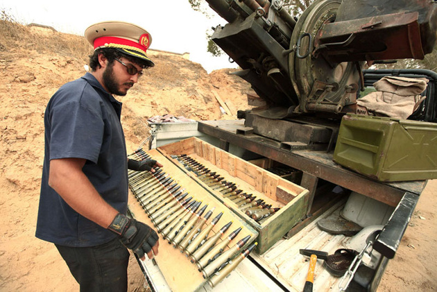 Ливийский повстанец в фуражке офицера армии Каддафи готовит боеприпасы для зенитной пушке, 25 км от центра города Мисрата.