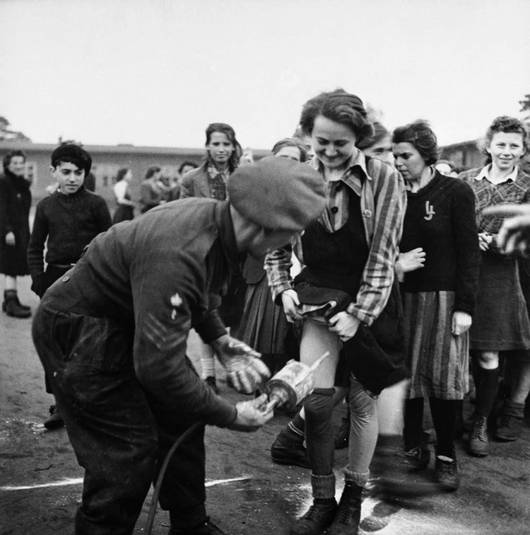 Британский сержант-медик проводит дезинфекцию бывших узниц концлагеря Берген-Бельзен. 1945