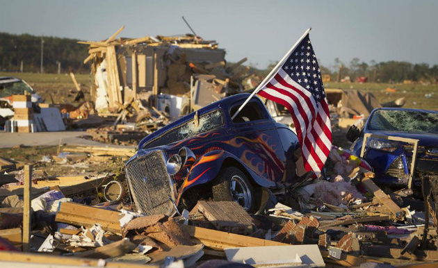© Carlo Allegri/Reuters. 
Американский флаг торчит из окна хот-род-автомобиля в пригородной зоне после торнадо недалеко от города Вилония, штат Арканзас
