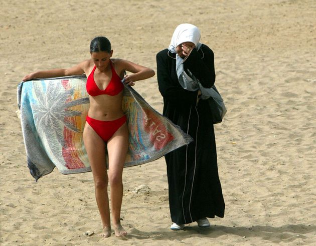 Девушка в бикини и ее подруга в традиционной одежде на пляже в Алжире, 25 июля 2003 года.