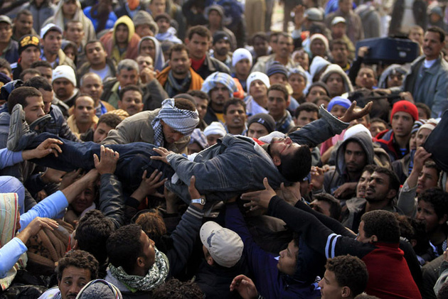 Египетские беженцы у тунисской границы несут на руках потерявшего сознание мужчину.