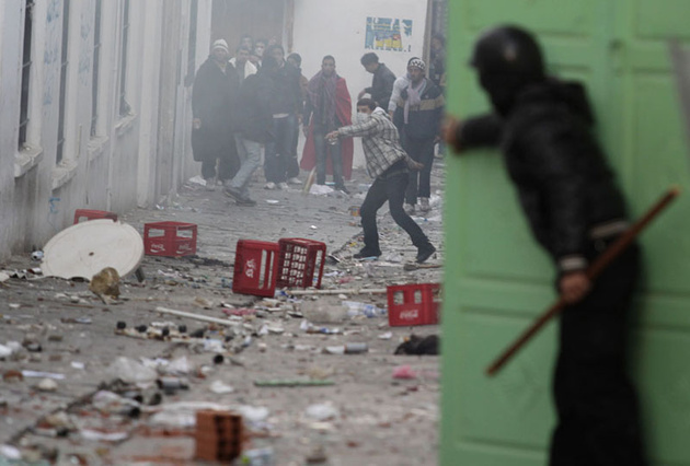 Полицейский укрывается за дверью от летящих камней, Тунис.