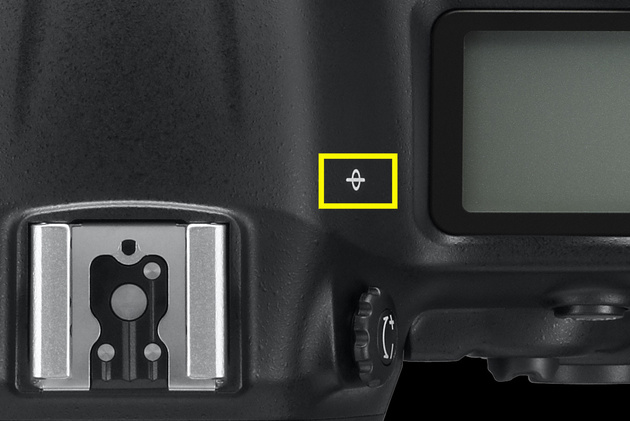 Таким значком на фотоаппарате обозначена фокальная плоскость, в которой находится матрица фотоаппарата. Именно от этого места отмеряют дистанцию фокусировки. 