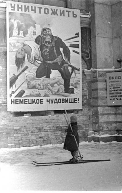 Ребенок на улице блокадного Ленинграда у плаката «Уничтожить немецкое чудовище!». 1942