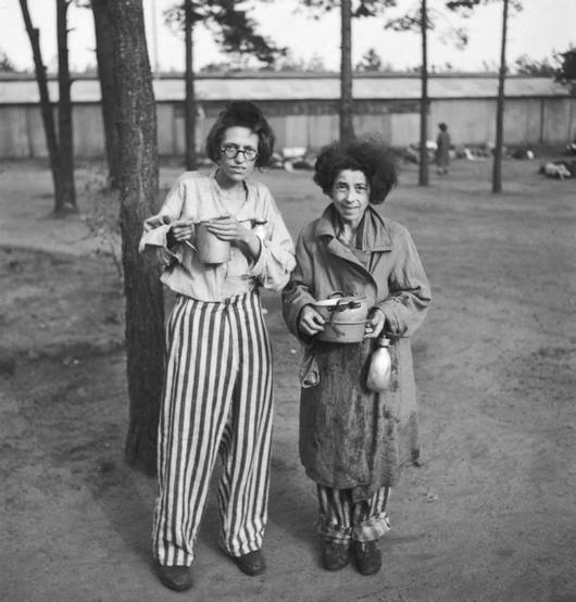 Две бывшие узницы Берген-Бельзена с посудой в лесу на фоне бараков. 1945